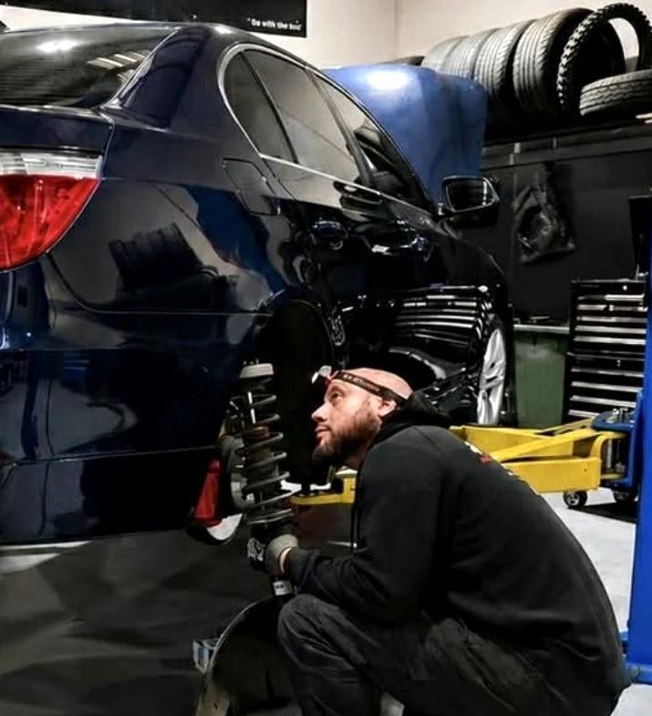 Technician working beside the exposed rear suspension of a blue BMW in the Autotech workshop