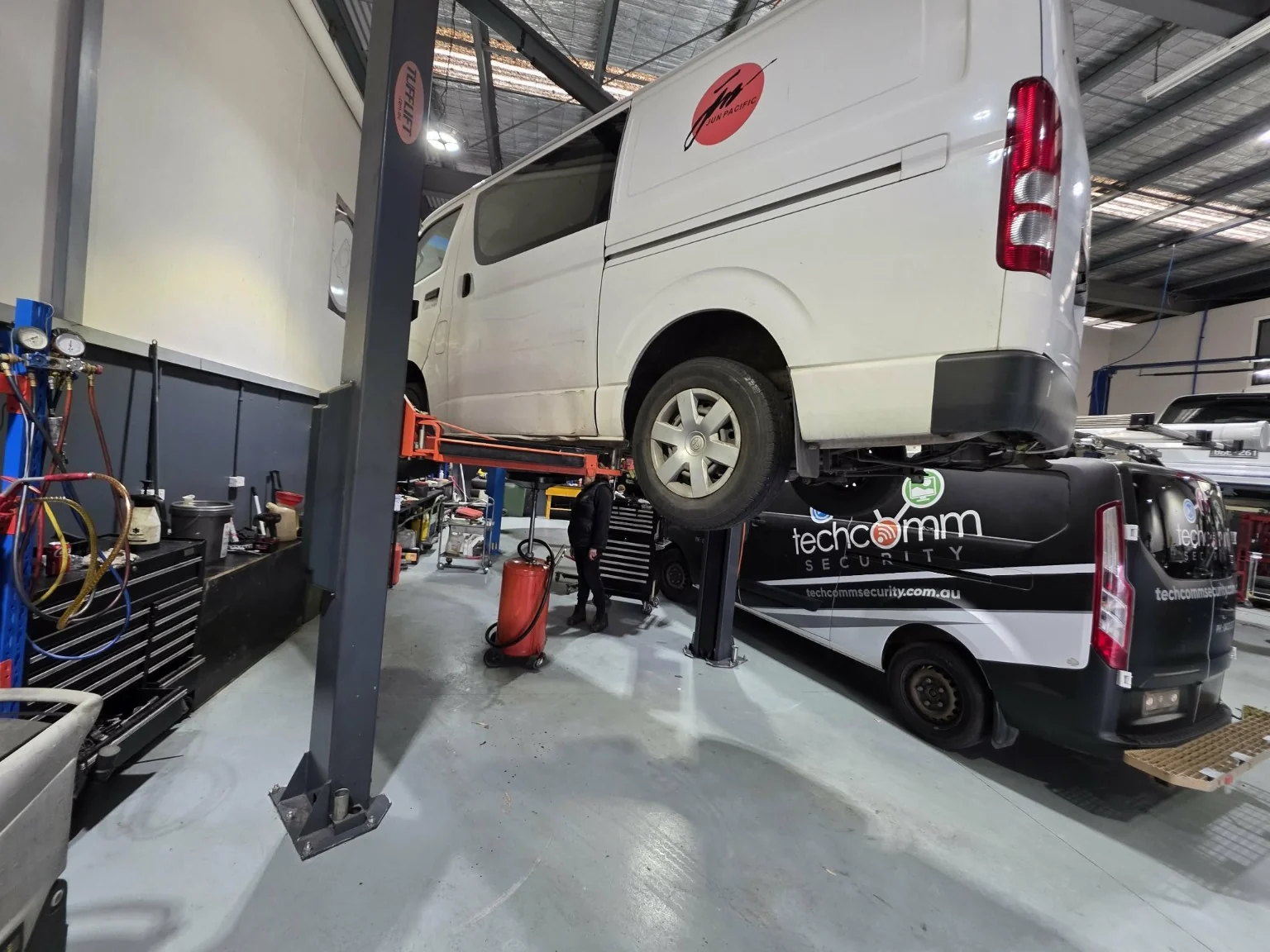 White commercial van raised on a hoist beside another van in the Autotech workshop